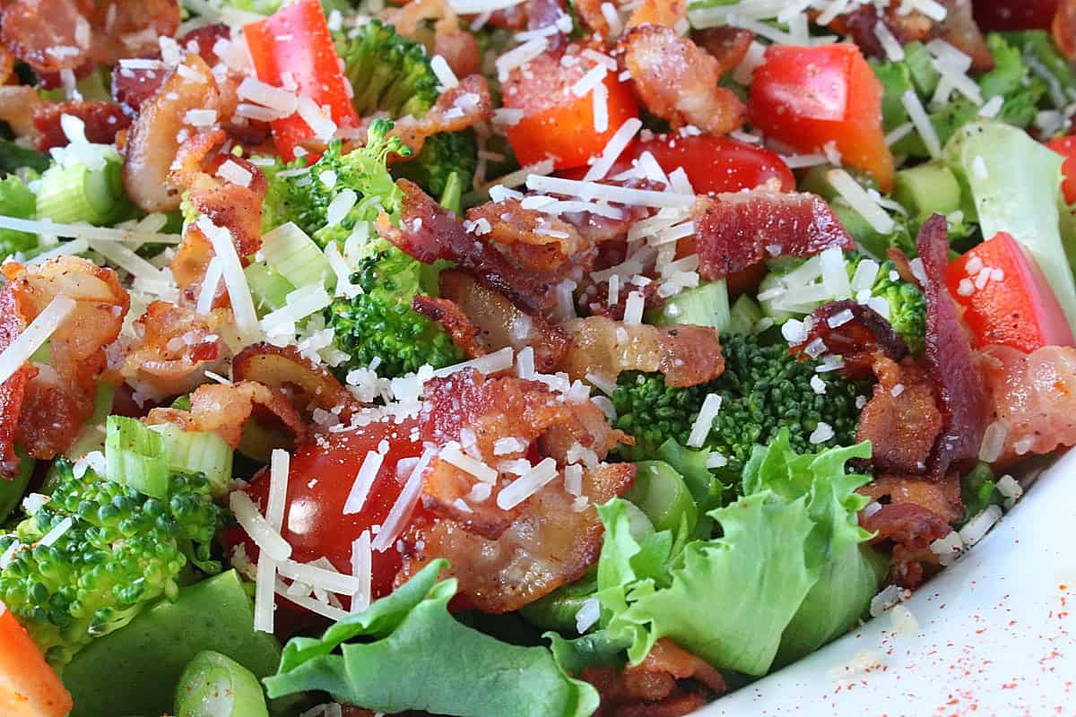 A salad topped with bacon, cheese, vegetables, and lettuces.