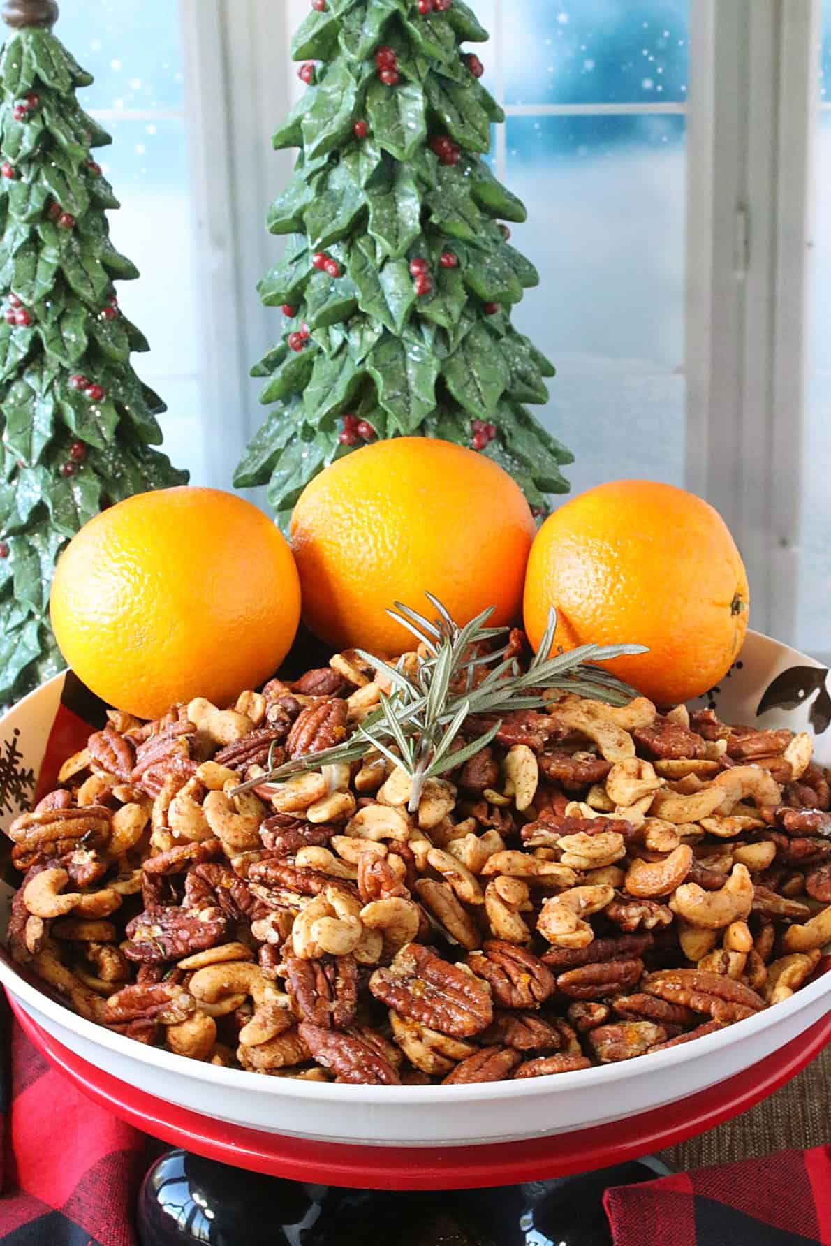 Three whole oranges in a bowl of cashews and pecans by a winter window.