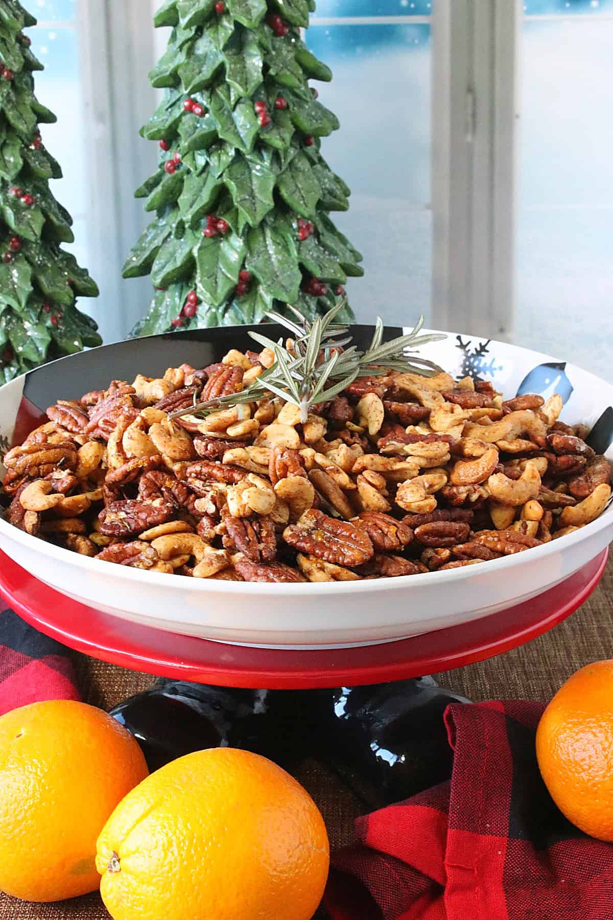A Christmas cake stand with a bowl of Orange and Herb Spiced Nuts on top.