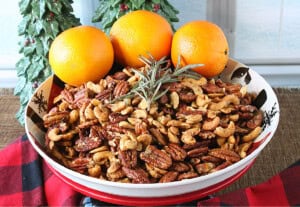 A delicious bowl of roasted pecans and cashews along with a sprig of rosemary and some fresh oranges.