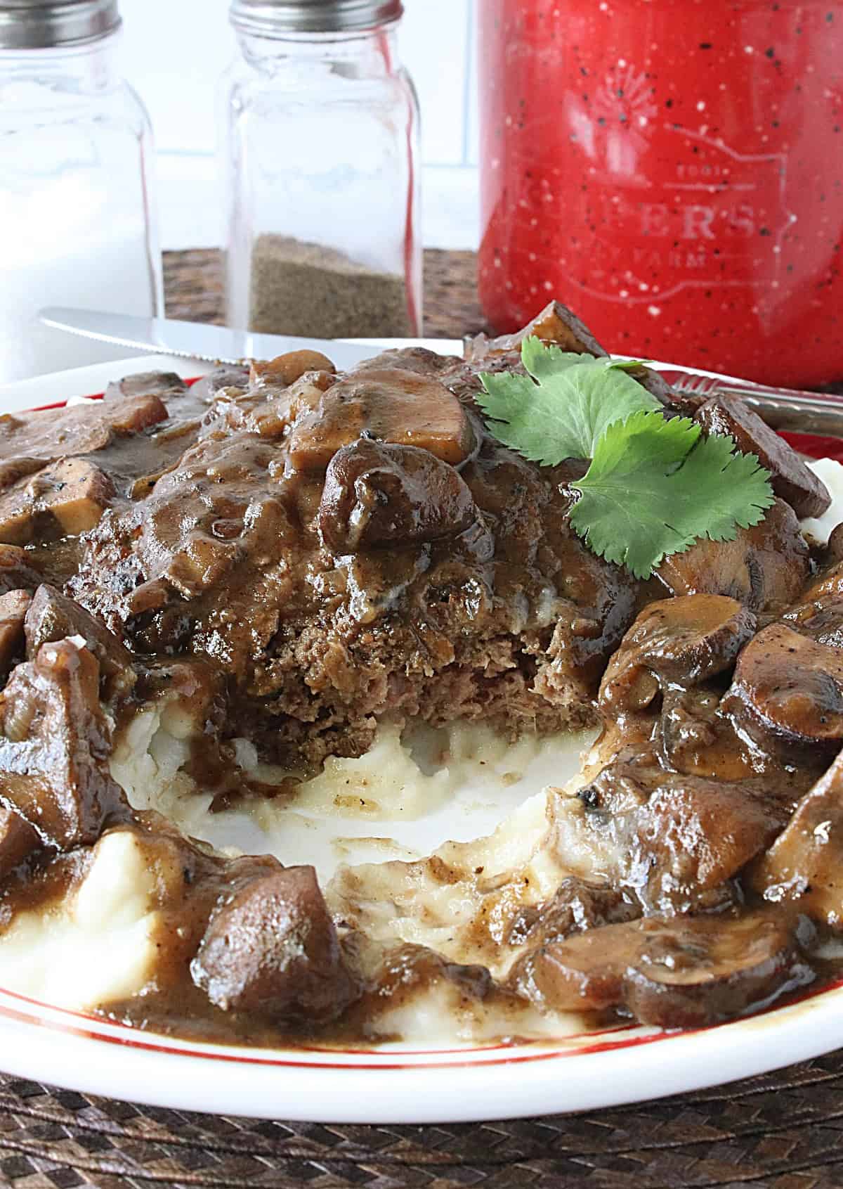 A ground beef patty covered with red wine mushroom gravy on a plate.