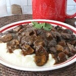 A red and white plate with a serving of ground beef salisbury steak covered in a deep brown mushroom gravy.