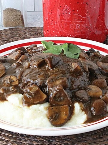 A red and white plate with a serving of ground beef salisbury steak covered in a deep brown mushroom gravy.