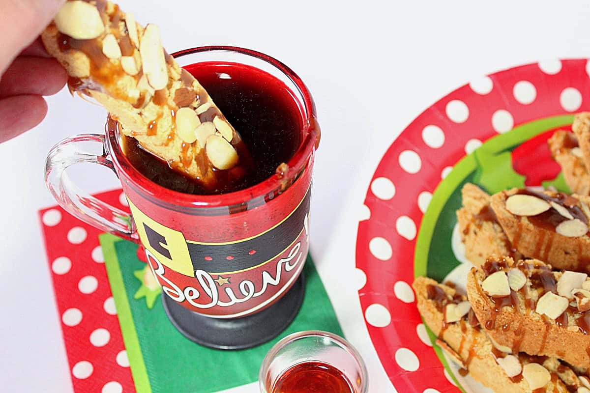 A hand dipping an Amaretto Coconut Biscotti into a cup of coffee.