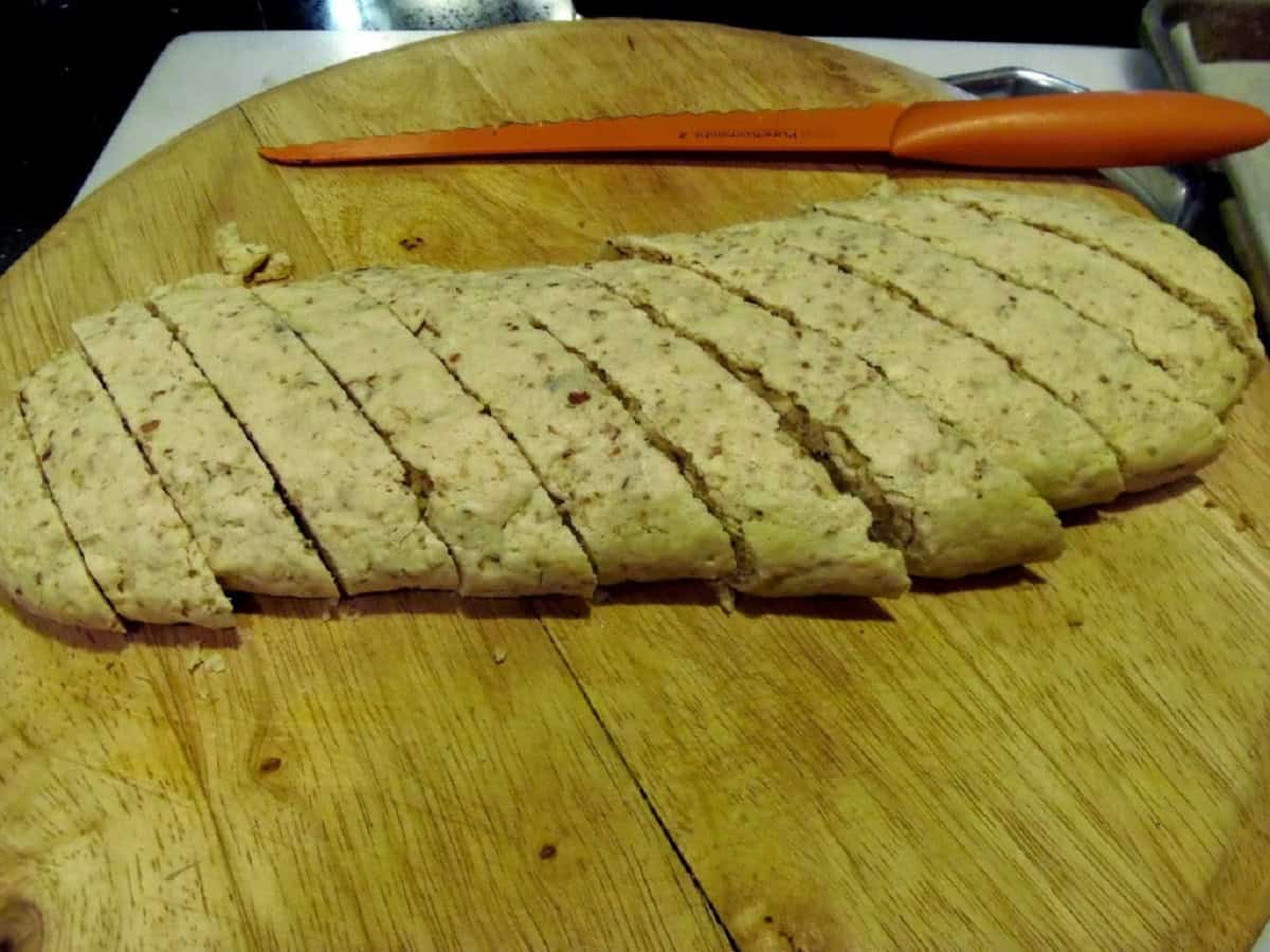 A log of baked biscotti cookies on a cutting board with a knife.
