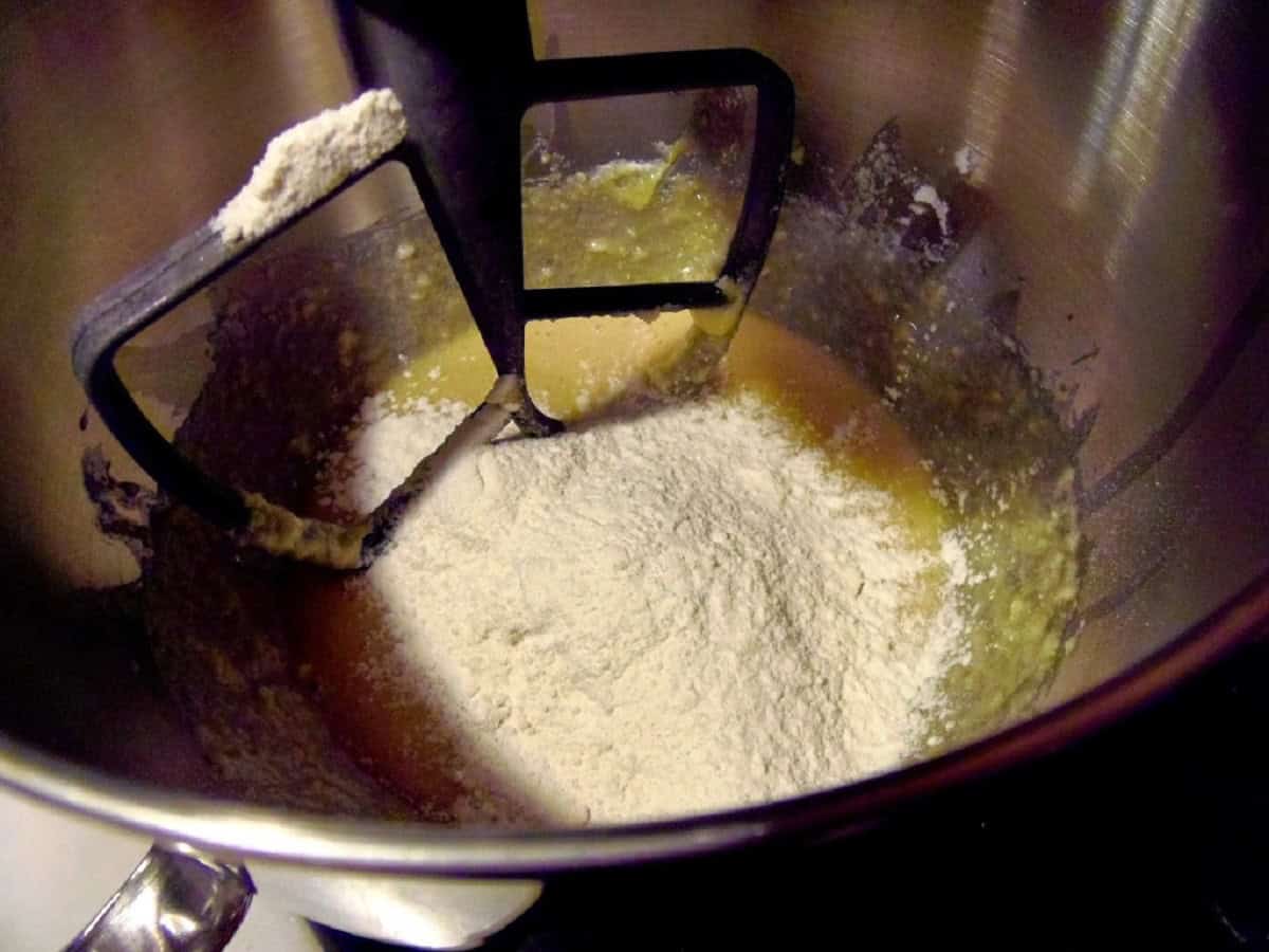 Flour added to wet ingredients in a bowl of a stand mixer.