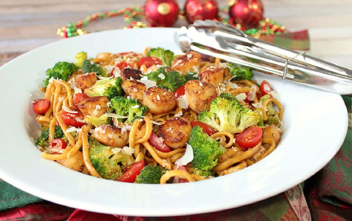 A pretty white bowl filled with scallops, pasta, broccoli and tomatoes.