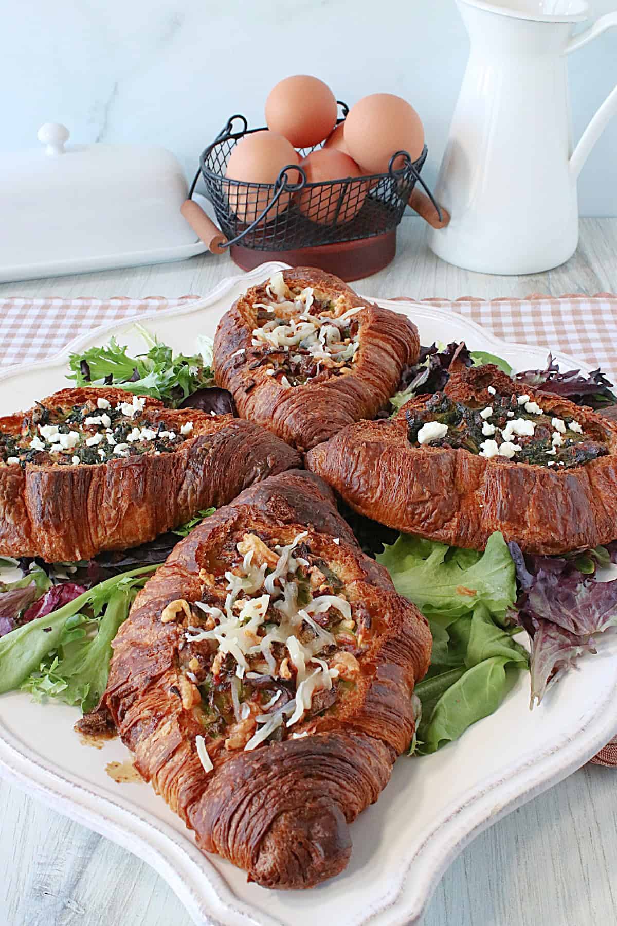 Four golden brown croissant and egg breakfast sandwiches on a square platter.