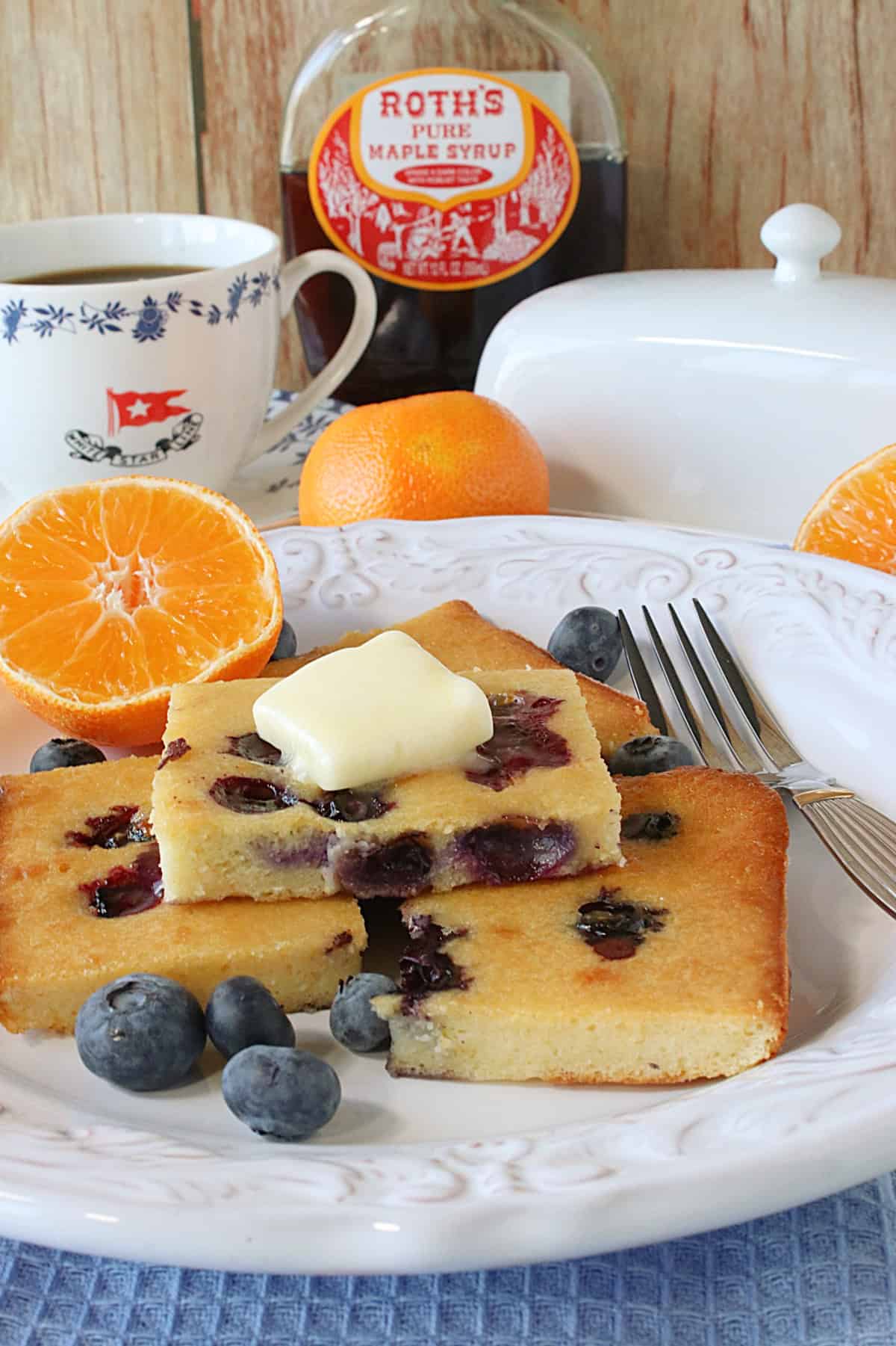 Coffee, butter, oranges, and maple syrup surrounding a plate of sheet pan pancakes.