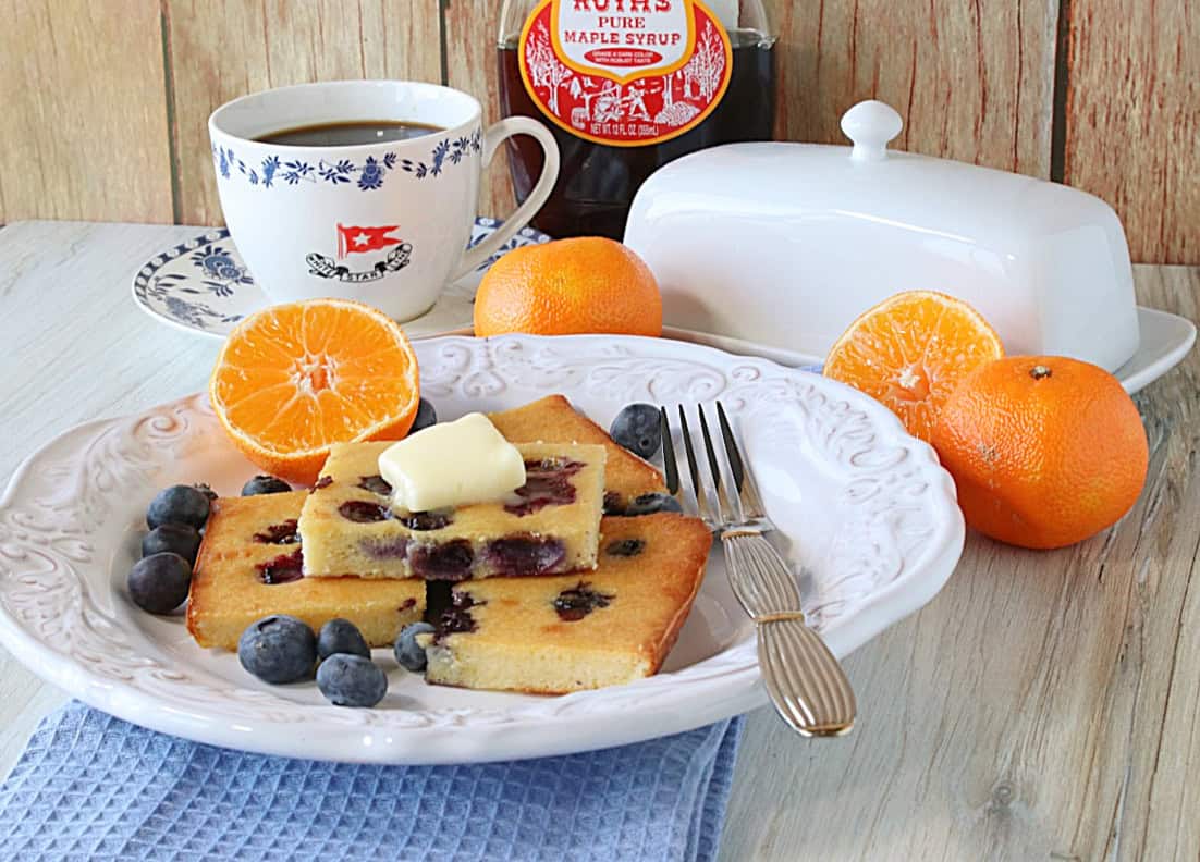 A table setting with sheet pan pancakes with oranges and blueberries on the plate.
