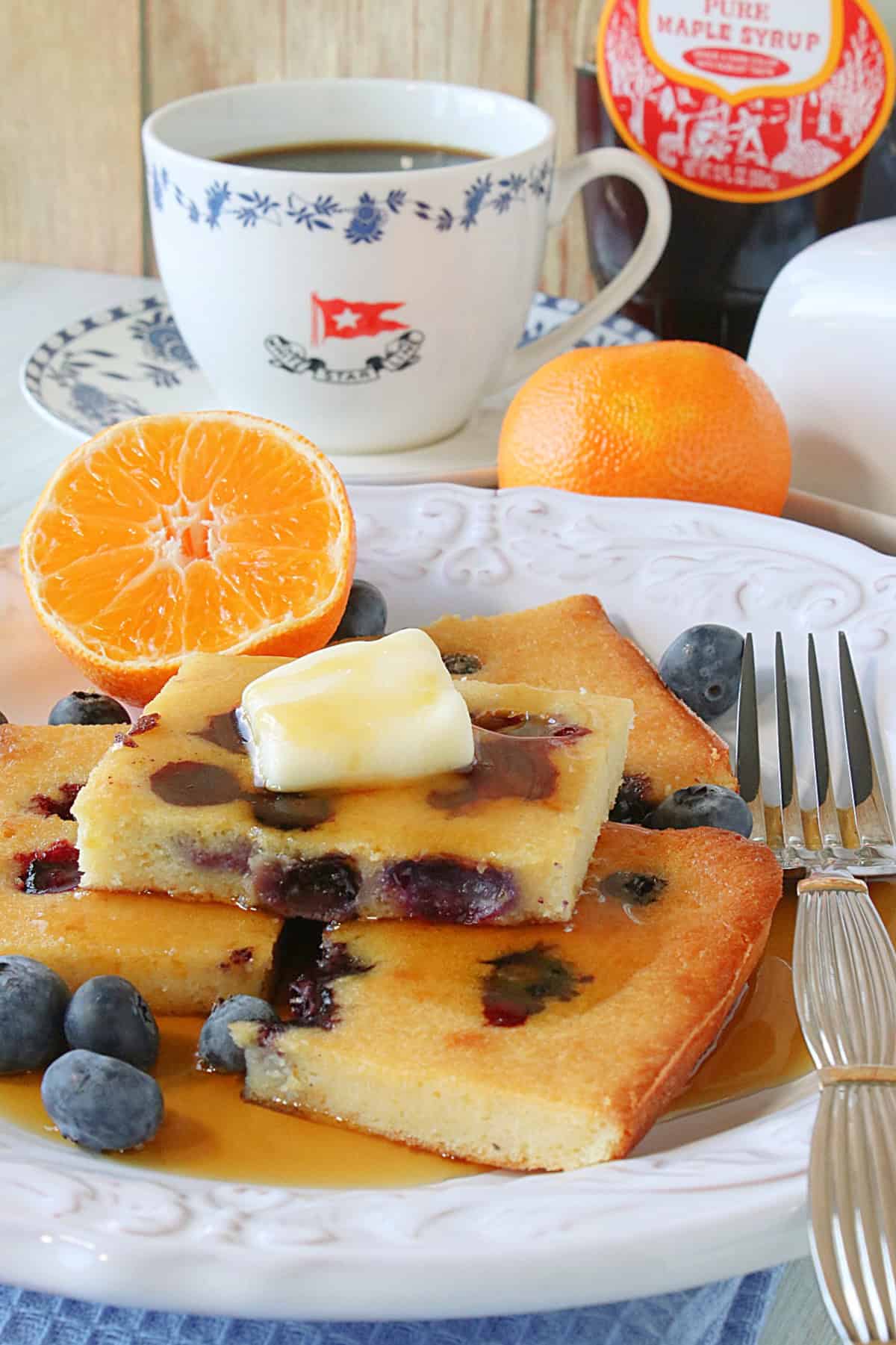 A stack of sheet pan pancakes with butter and syrup on a white plate.