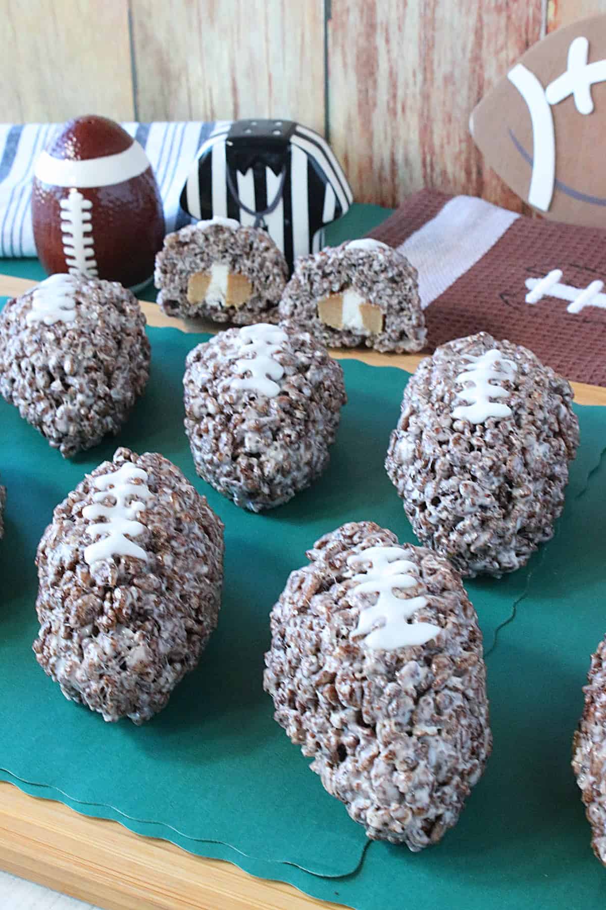 Whole cocoa krispies football treats in the foreground and one cut in half showing the caramel cream center in the background.