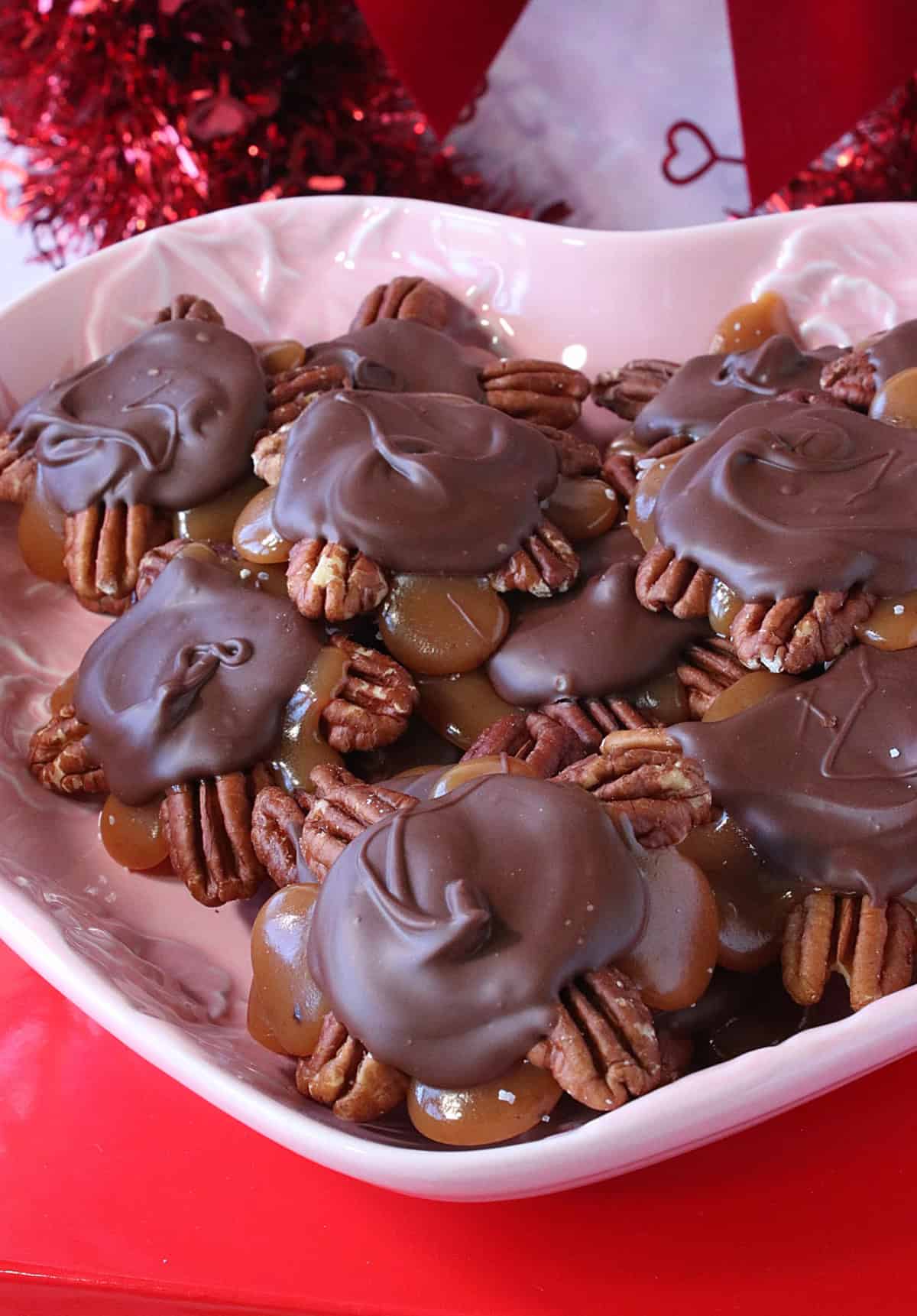 A pink dish with caramel, chocolate, and pecan turtles.