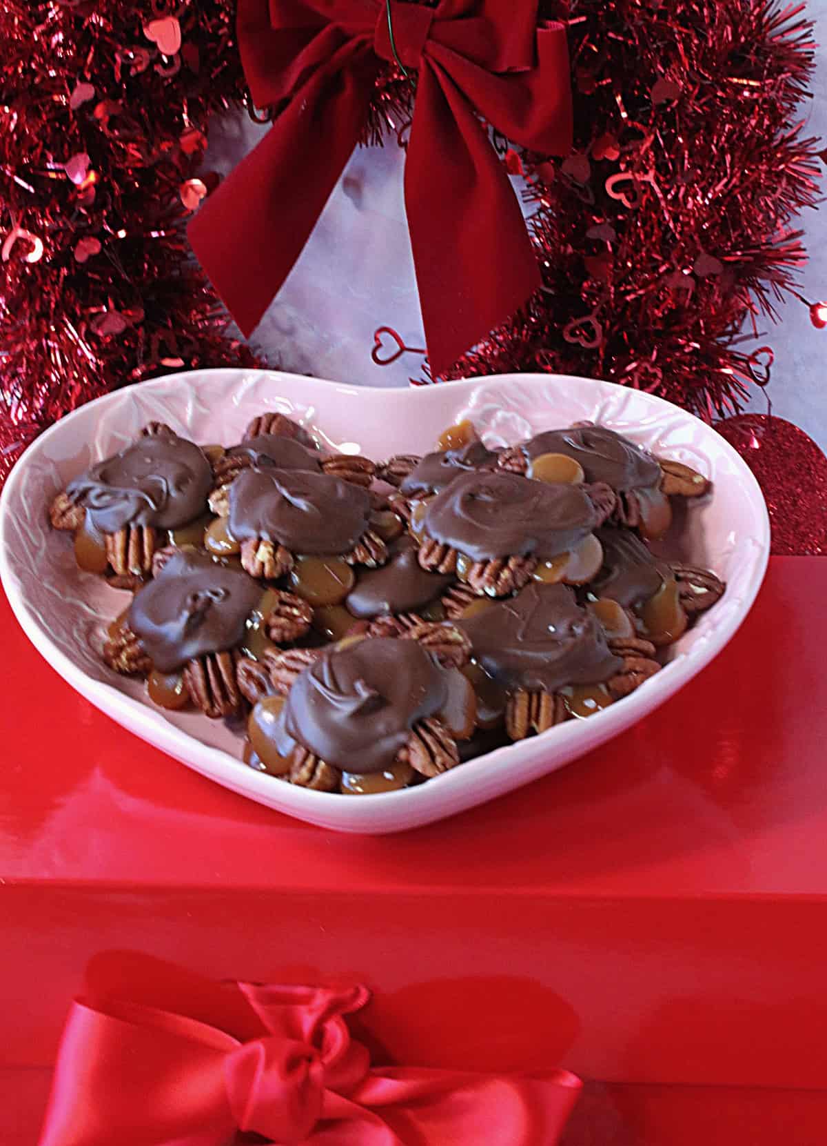 A dish of turtle candy sitting on a red box with a bow for Valentine's Day.