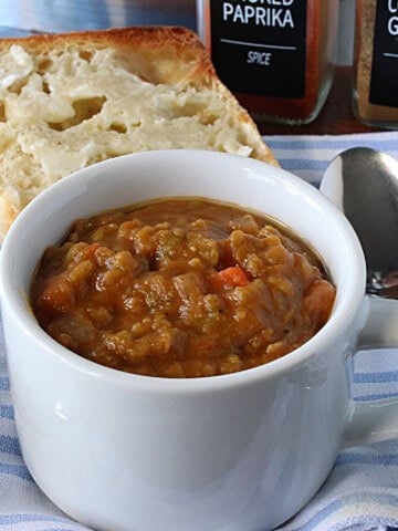 A delicious looking mug of Slow Cooker Split Pea Soup with Ham Hocks with a spoon on the side.