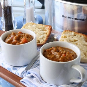 Two white mugs filled with split pea soup along with some toasted bread in the background.