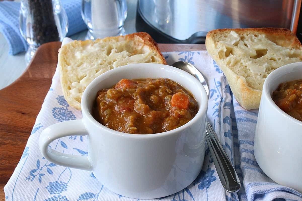 A white cup of slow cooker split pea soup with ham hocks.