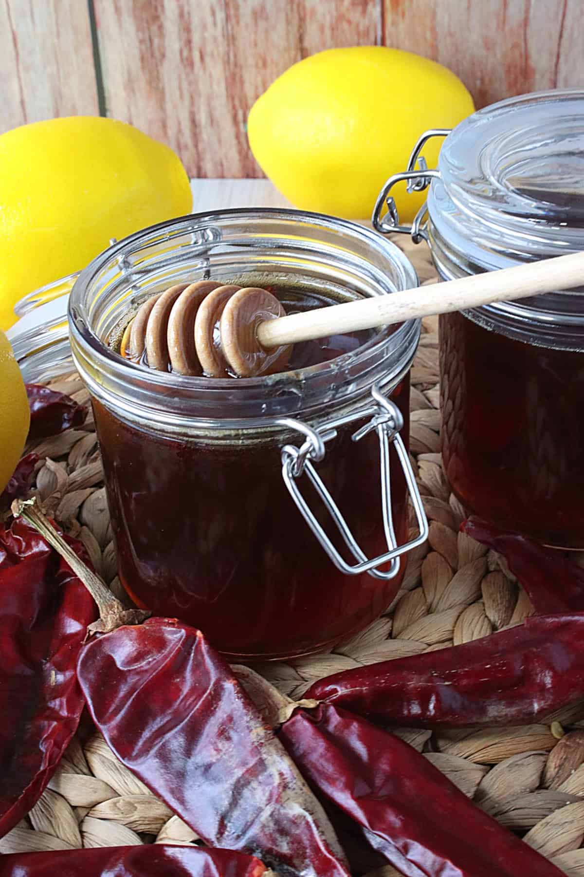 Dried peppers and lemons around a jar of hot honey with a wooden dipping stick in the jar.