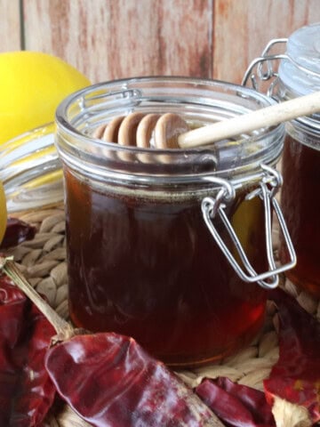 A jar of hot honey with lemons and dried peppers surrounding it.