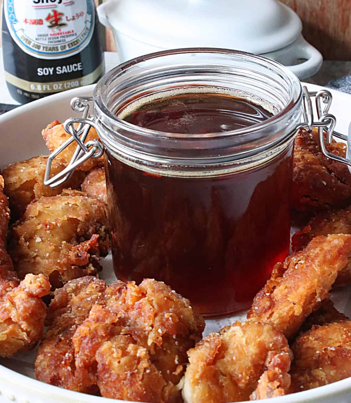 A jar of sweet and sour hot pepper honey in the center of a bowl of chicken nuggets.