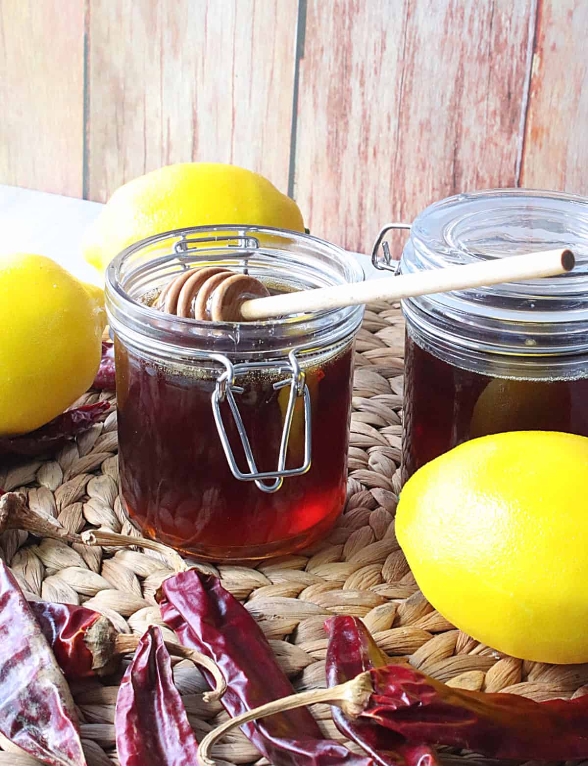 Dried peppers and lemons surrounding a jar or hot honey.