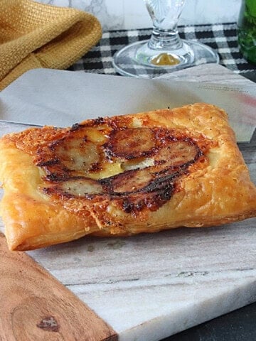 A puffed pastry bratwurst and cheese square on a marble tray.