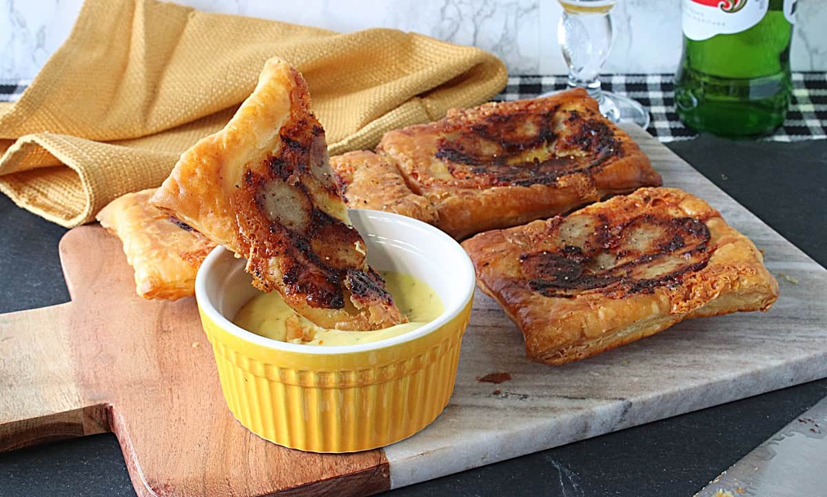 A marble serving board with puff pastry brat and cheese appetizers.
