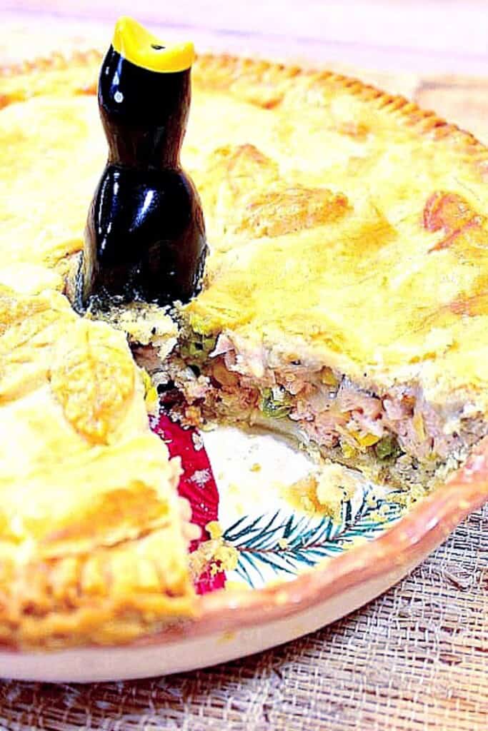 A Pork Pot Pie with a slice taken out along with a pie bird in the center.