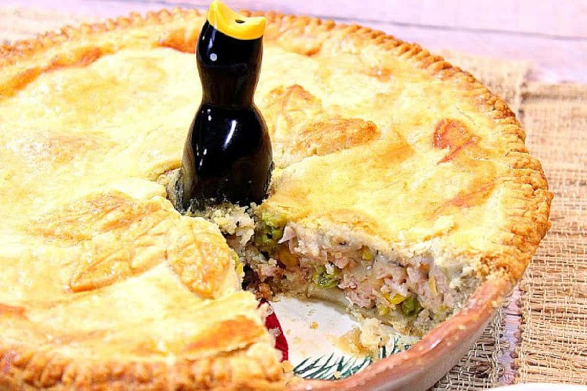 A golden homestyle pork pot pie with a slice taken out and a pie bird in the center.
