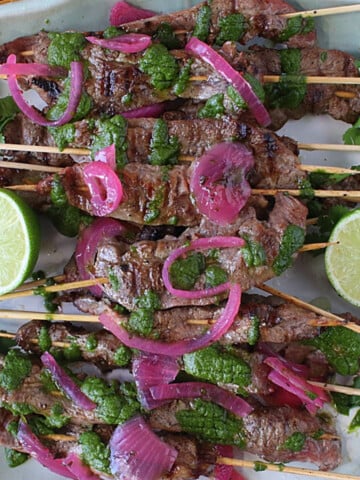 Skewered beef flank steak on a platter topped with chimichurri sauce.