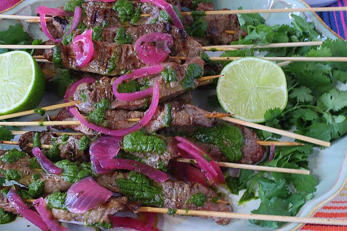 Wooden skewers with grilled flank steak on a bed of cilantro and topped with red onion.