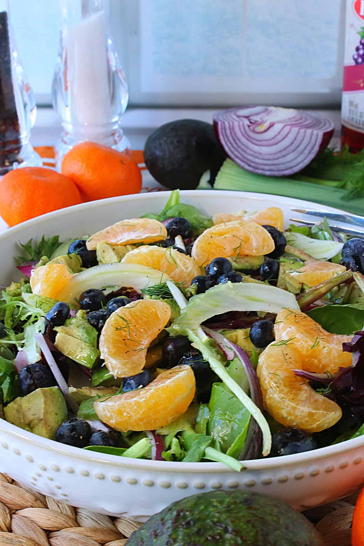 A pretty white bowl filled with salad containing fresh fennel, orange, and blueberries.