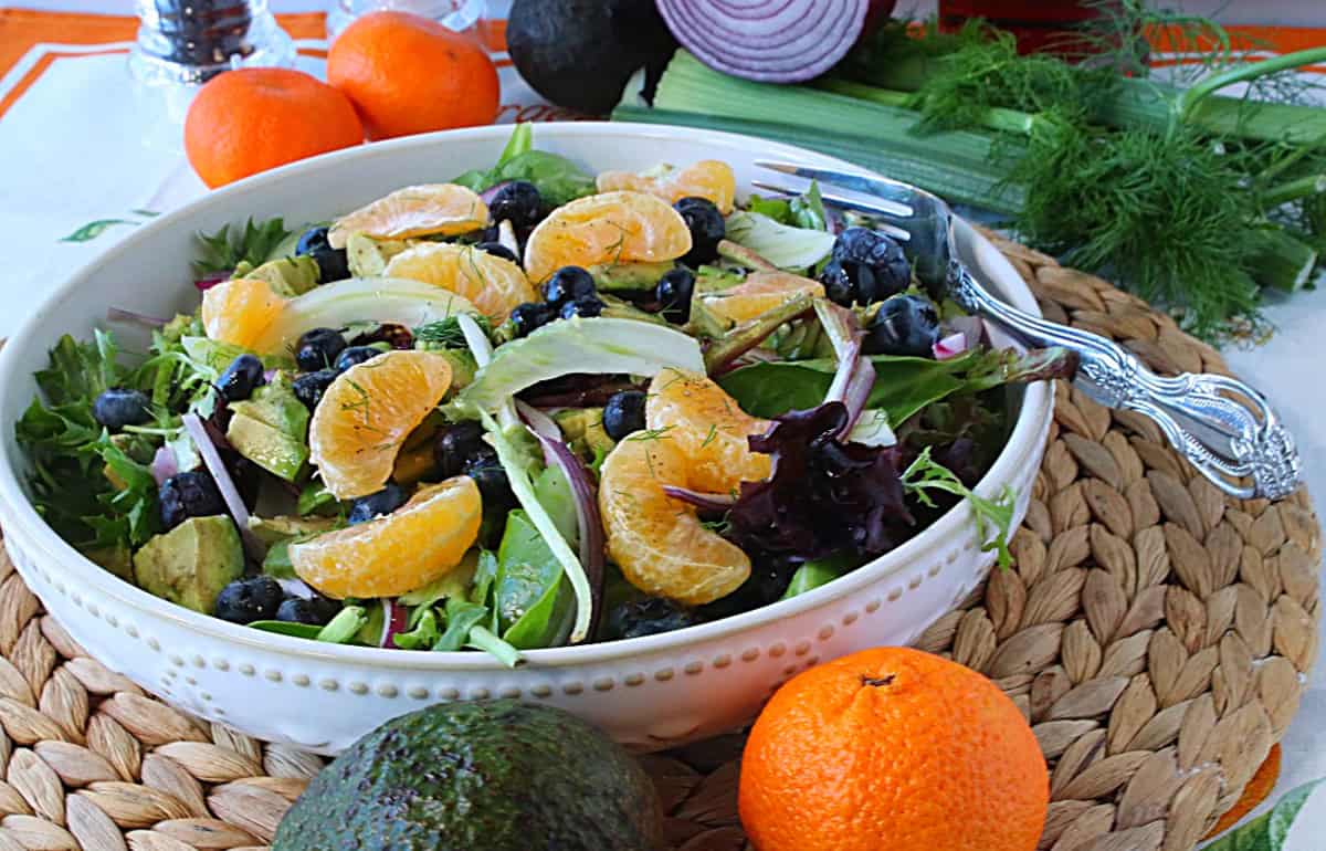 A white bowl filled with a colorful fresh fennel salad with orange segments and blueberries.