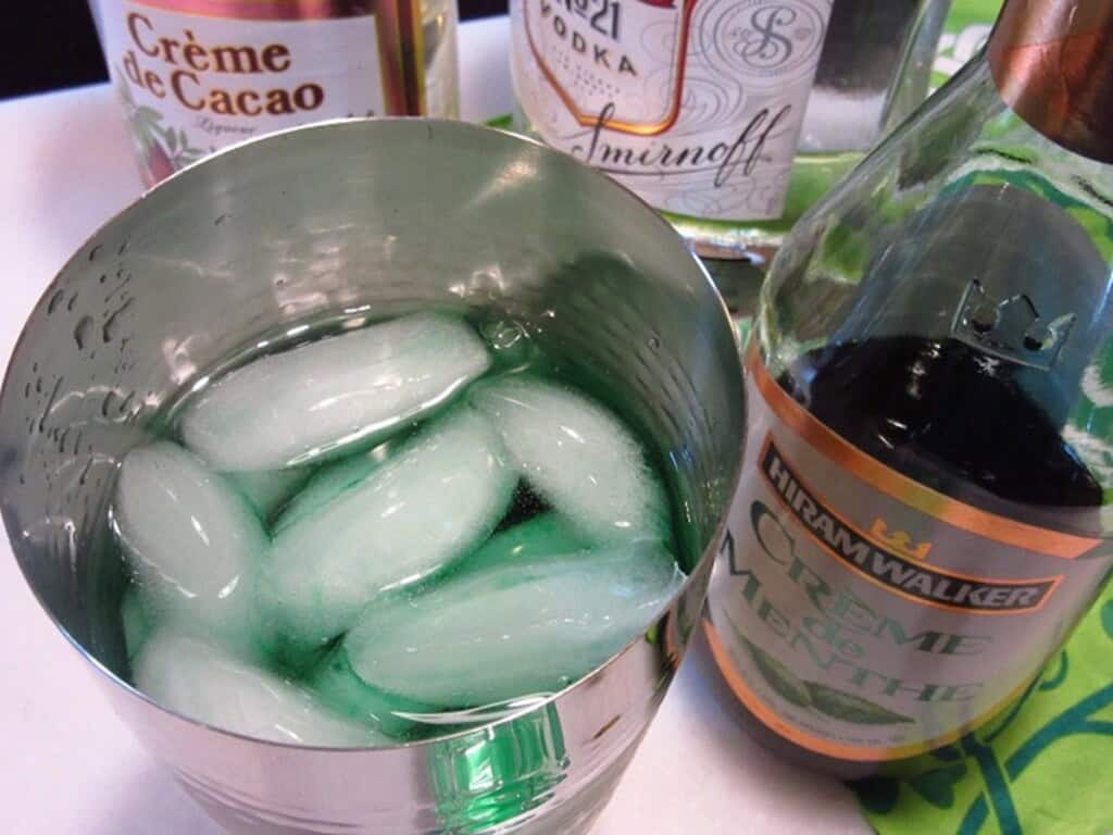 Ice and creme de menthe in a cocktail shaker.