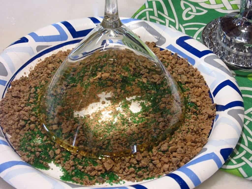 A martini glass being rimmed in green sugar and cocoa.