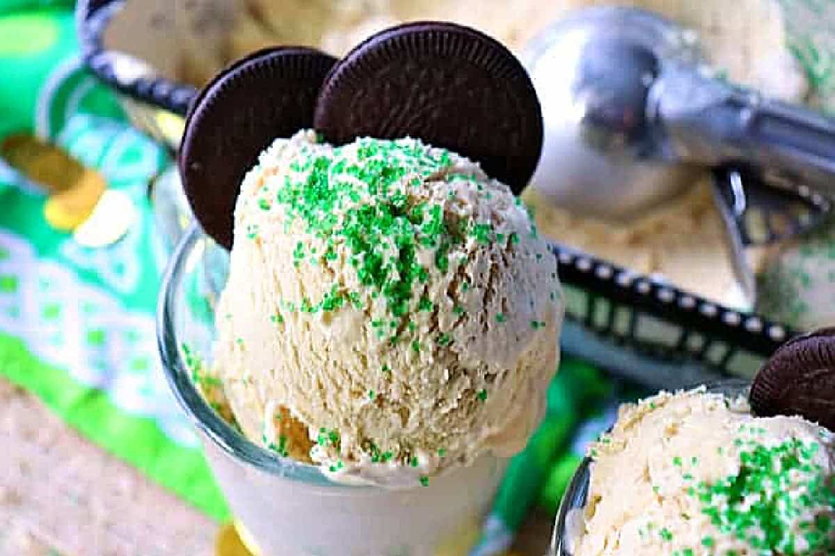 A scoop of ice cream with green sugar and two cookies on top.