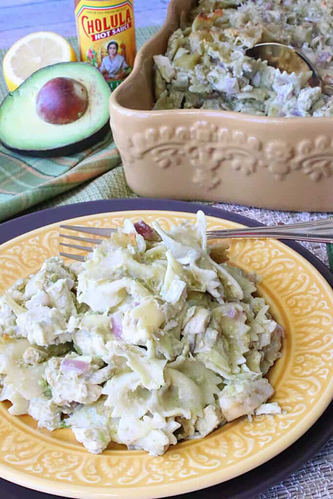 Bow tie pasta with chicken, artichokes, and avocados on a serving plate with a fork.