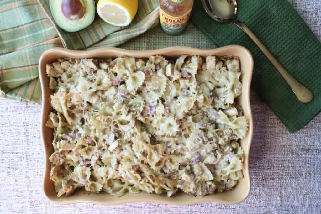 A rectangle casserole dish filled with chicken artichoke pasta with avocados and a green napkin.