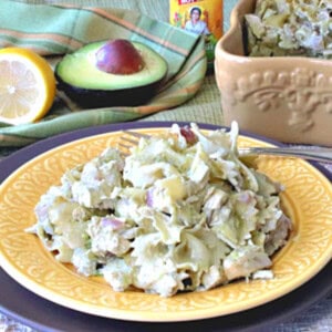 A yellow plate with a serving of chicken artichoke pasta and a fork.