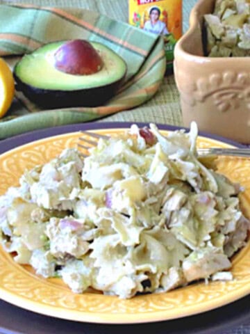 A yellow plate with a serving of chicken artichoke pasta and a fork.
