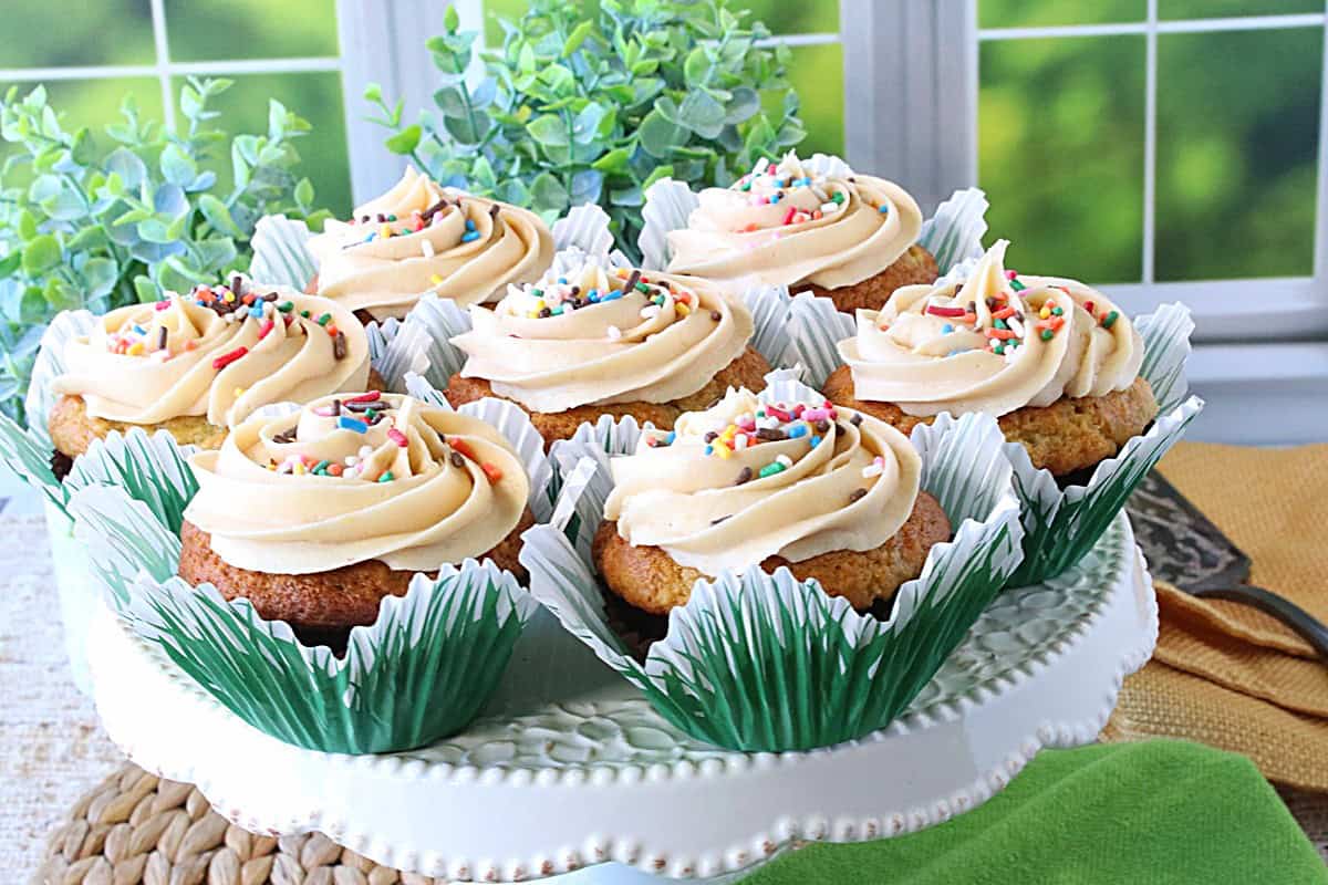 A pretty bunch of cupcakes with swirly frosting and sprinkles on a cake plate.