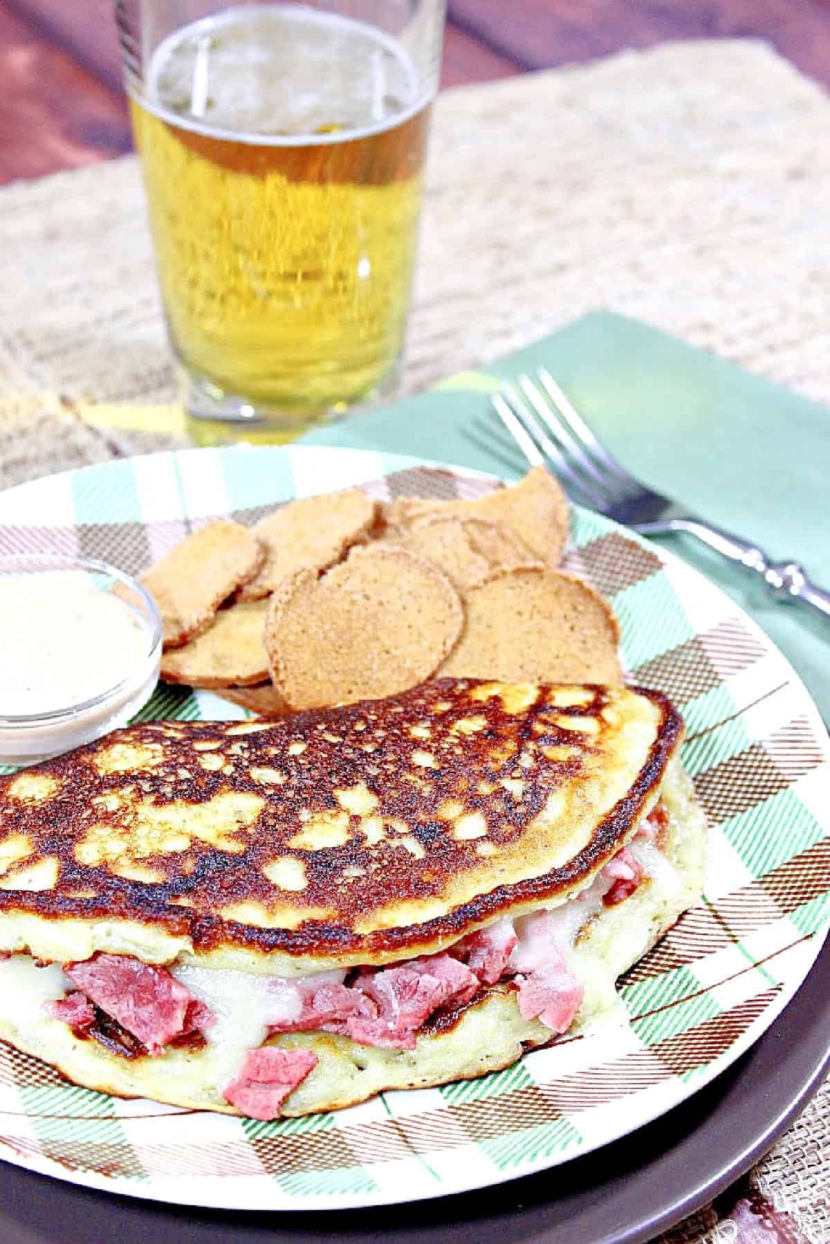 A tall glass of beer behind a plaid plate with an Irish Corned Beef Boxty.