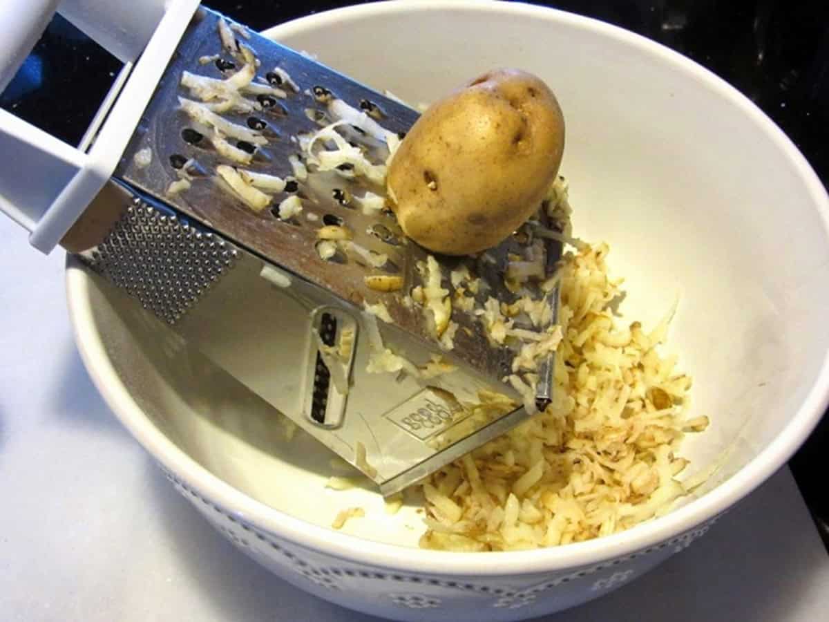 A Yukon gold potato being grated into a bowl