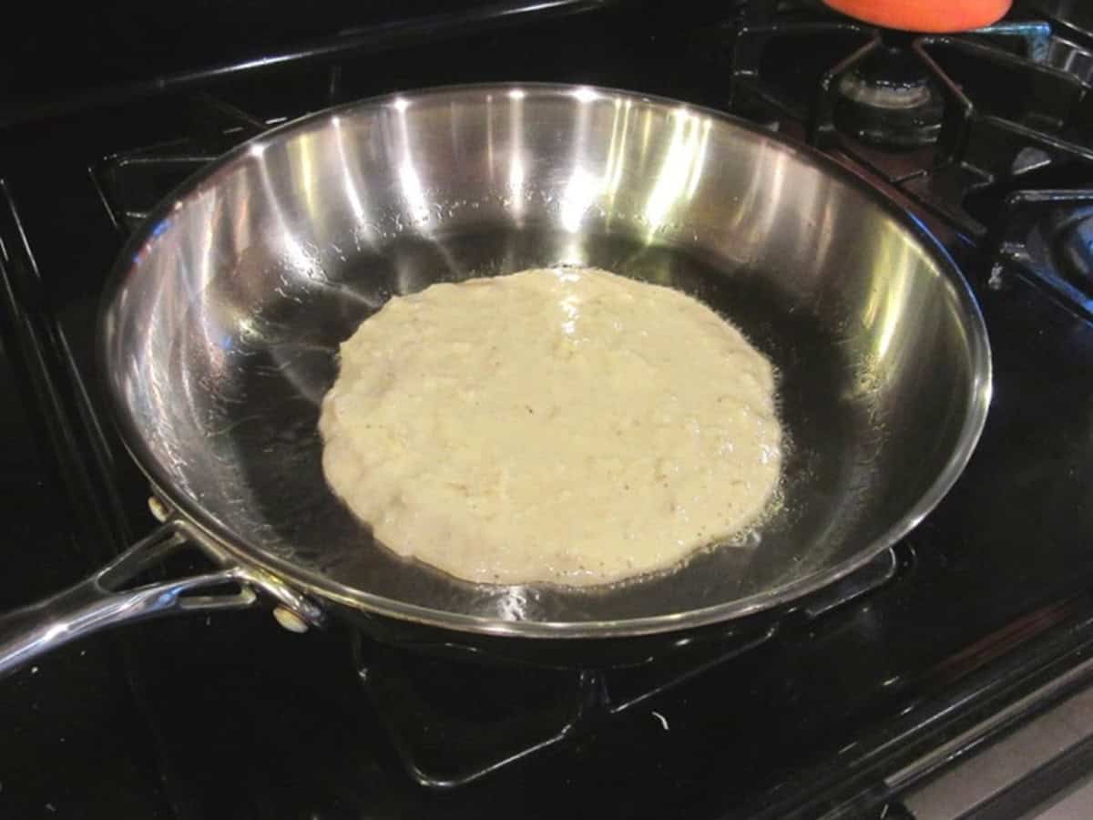 A potato pancake in a skillet before flipping.