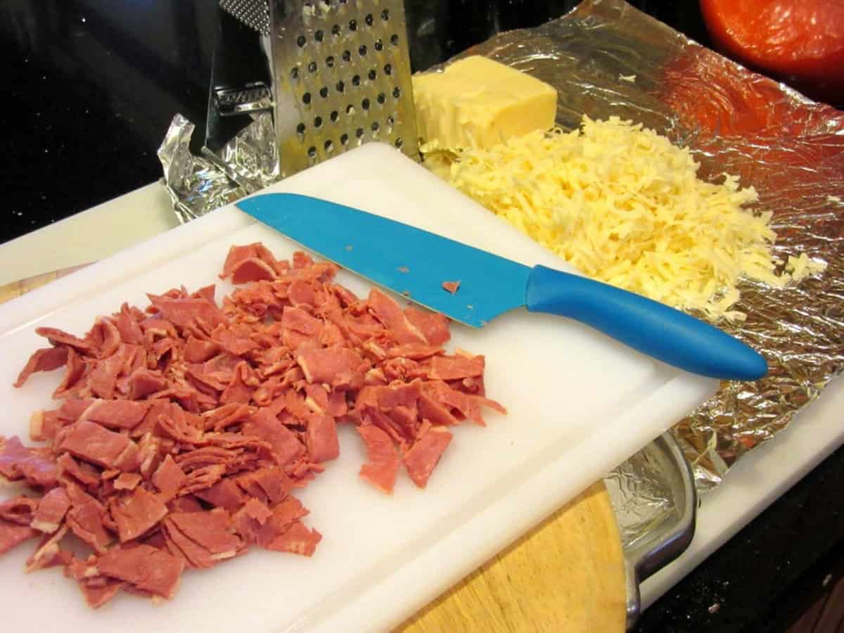 Chopped corned beef on a cutting board with shredded Swiss cheese on some foil.