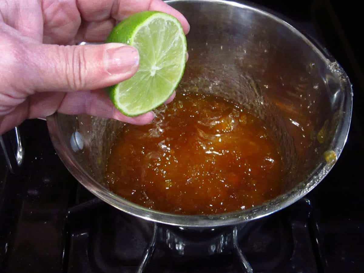 Fresh lime juice being added to a saucepan with apricot jam.