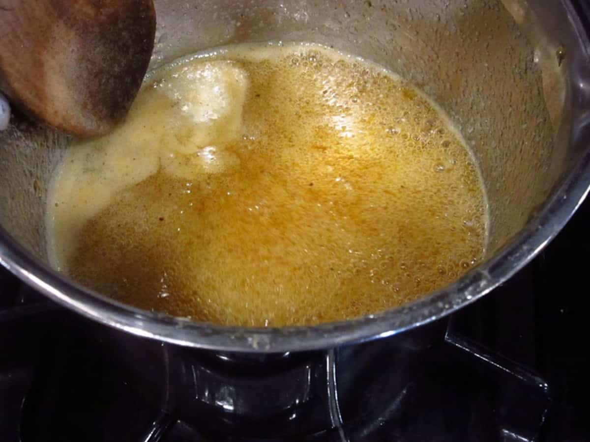 A bubbling whiskey sauce with wooden spoon in a saucepan.