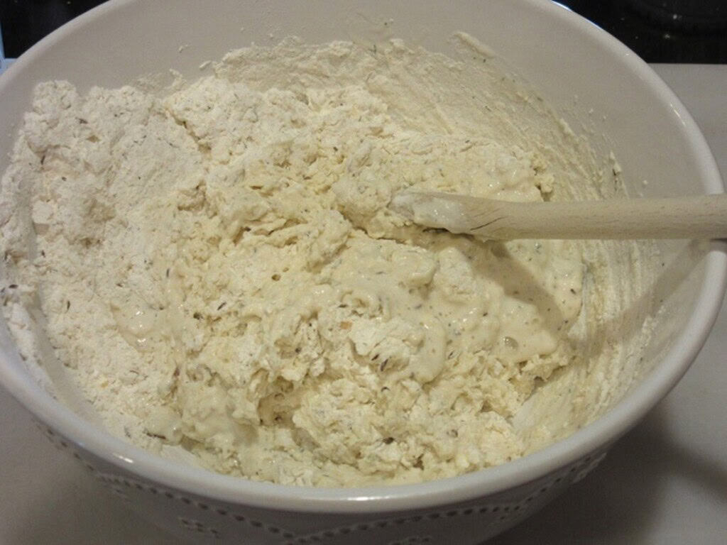 The mixing of Irish soda bread in a white bowl with a wooden spoon.