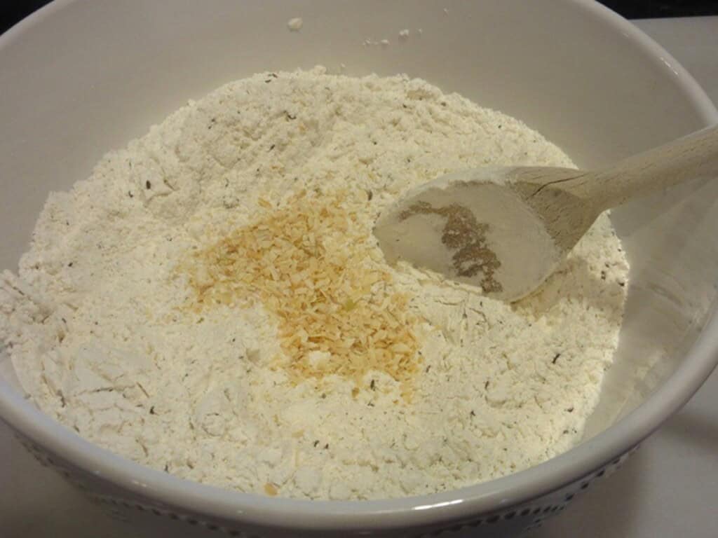 Flour and dehydrated minced onions in a white bowl with a wooden spoon.