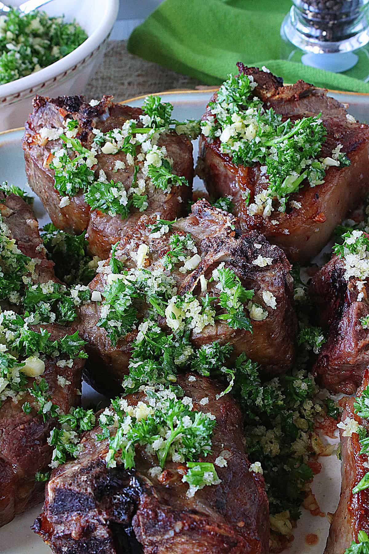 Bone in lamb chops on a dinner platter topped with green parsley persillade and panko crumbs.